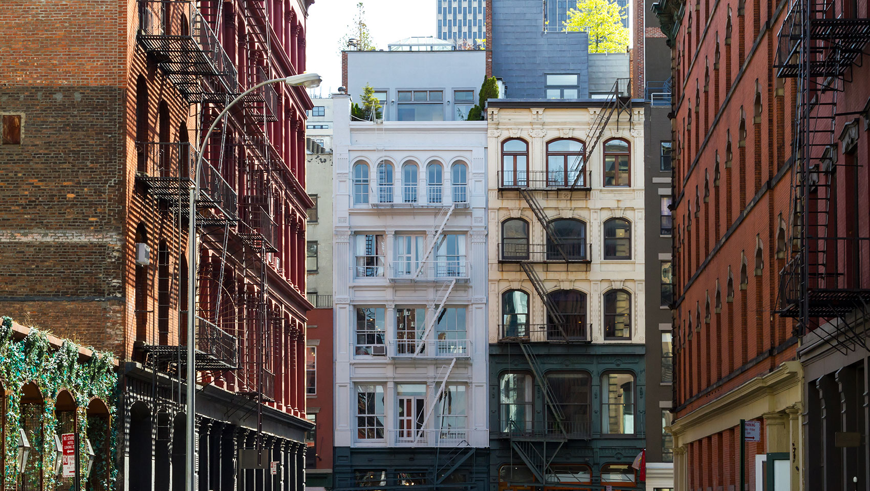 Urban street with brick buildings and fire escapes, leading to three distinct buildings with rooftop gardens.